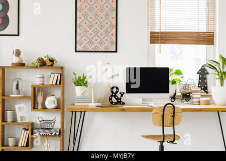 Photo réelle d'un bureau avec un écran d'ordinateur, lampe et ornements debout avec une chaise à côté de la grille d'une salle de travail avec des affiches sur un mur et fenêtre Banque D'Images