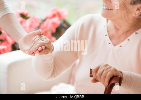 Close-up of caregiver soutenir smiling senior woman with walking stick Banque D'Images