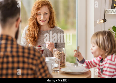 Jeune famille manger le petit déjeuner ensemble dans une salle de séjour avec grande fenêtre Banque D'Images