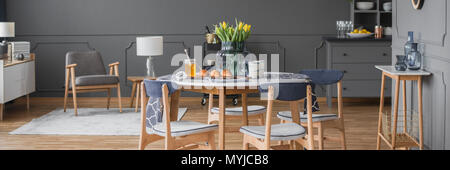 Fauteuil en bois gris à l'intérieur de l'espace ouvert avec des chaises à table à manger ronde avec des fleurs jaunes Banque D'Images