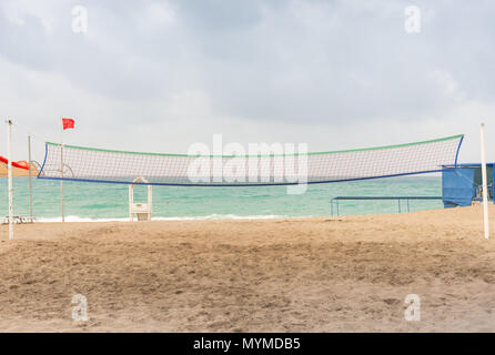 Filet de volley-ball sur une plage tropicale avec des traces de pas dans le sable et un océan calme sous un ciel nuageux Banque D'Images