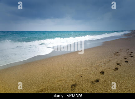 Ligne d'empreintes de pas dans le sable sur une plage déserte menant de l'appareil photo au bord de l'océan calme avec un surf Banque D'Images
