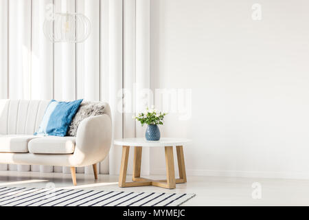 Table en bois blanc, à côté du canapé avec coussin bleu au mur vide intérieur de salon Banque D'Images