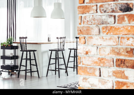 Mur de briques rouges dans salle à manger rustique avec lampes blanches au-dessus de comptoir avec tabourets de bar noir Banque D'Images