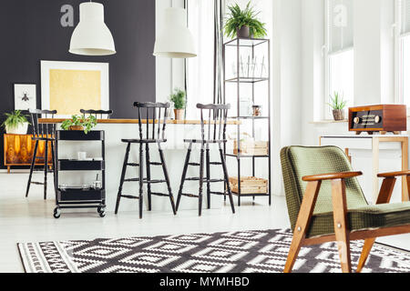 Fauteuil vert rustique sur noir et blanc tapis géométriques dans la cuisine avec tabourets de bar au comptoir Banque D'Images