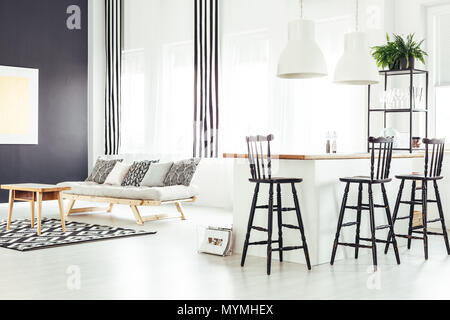 Oreillers beige à motifs sur canapé avec table en bois sur tapis géométriques dans la salle avec comptoir et tabourets de bar Banque D'Images