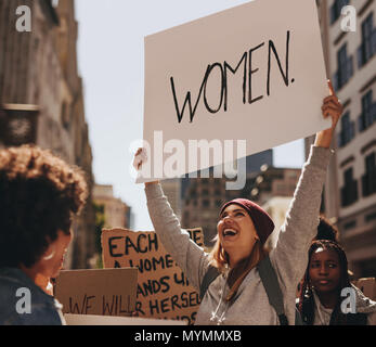 Happy young woman signe de protestation écrite à la Marche des femmes. Groupe de femelles démontrant l'extérieur. Banque D'Images