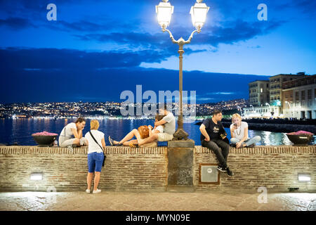 Des gens assis sur mur sous lampe de rue par le Castel dell'Ovo au crépuscule, Naples, Campanie, Italie, Europe Banque D'Images