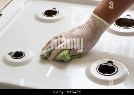 Femme main dans un gant avec un chiffon pour nettoyer la cuisinière à gaz sale Banque D'Images