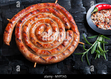 Grillades de saucisses en spirale sur fond noir de charbon de bois. Banque D'Images