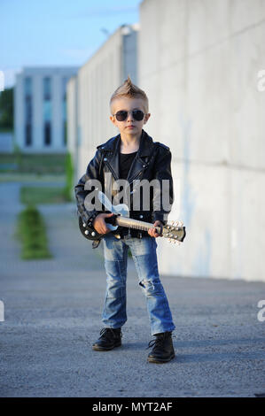 Un petit garçon mignon, guitariste de blouson de cuir et lunettes de jouer de la guitare. L'idole des jeunes. L'intérêt de l'enfant et passe-temps. Être comme une rock star. Banque D'Images