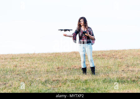 Young woman holding up drone caméra vidéo contrôle à l'automne ou à l'automne avec des bottes en campagne en Virginie parc open field hill Banque D'Images