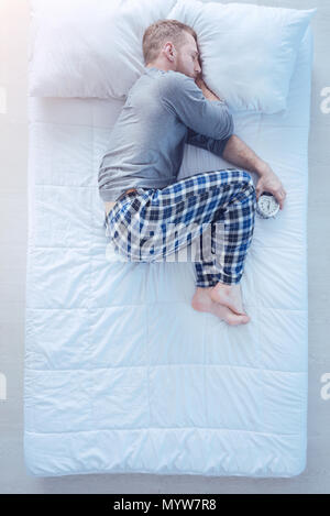 Homme avec réveil de dormir dans la position fœtale Banque D'Images