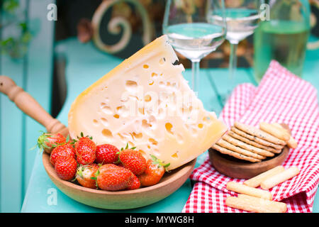 Fromage avec des trous et de fraises. Vin blanc dans un verre et des collations. La nourriture sur le balcon. Vue du dessus . Place pour le texte. Fleurs et plantes près de la table. Banque D'Images