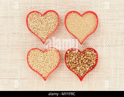 Quatre coeurs rouges remplis de graines de super santé quinoa, millet, amarante et de sarrasin sur toile Banque D'Images