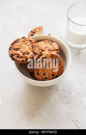 Des cookies aux pépites de chocolat dans un bol et verre de lait frais sur un fond noir en blanc. Banque D'Images