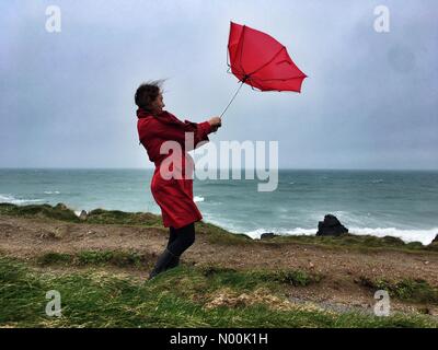 Météo France : Jour de vent pour parasols colorés à St Ives. Raich Keene combat de fortes rafales de vent avec son parapluie sur la côte de St Ives. Banque D'Images