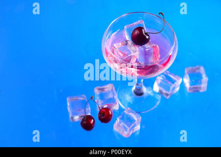 Le verre à champagne avec les glaçons et cerises de ci-dessus, sur un fond bleu. Boisson fraîche mise à plat avec copie espace Banque D'Images