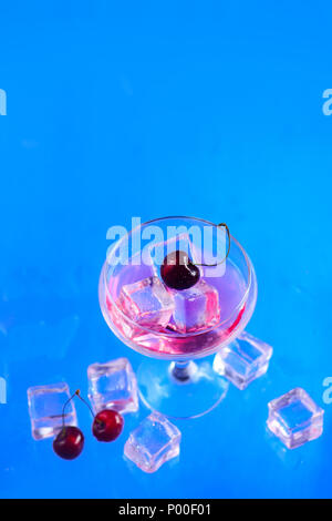 Le verre à champagne avec les glaçons et cerises de ci-dessus, sur un fond bleu. Boisson fraîche mise à plat avec copie espace Banque D'Images