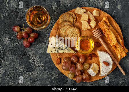 Assortiment de fromage avec du vin, du miel, des noix et du raisin sur une planche à découper, vue du dessus. Banque D'Images