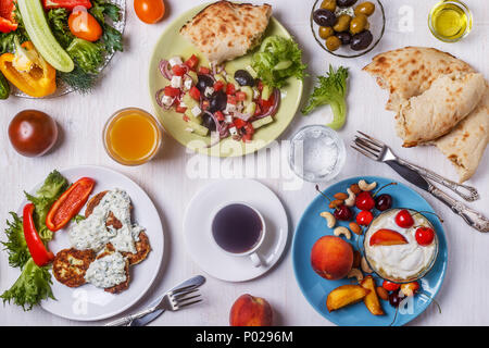 Apéritifs grecs - beignets de courgette avec sauce tzatziki, salade grecque, yaourt aux fruits et noix, olives, légumes et fines herbes, vue d'en haut. Banque D'Images