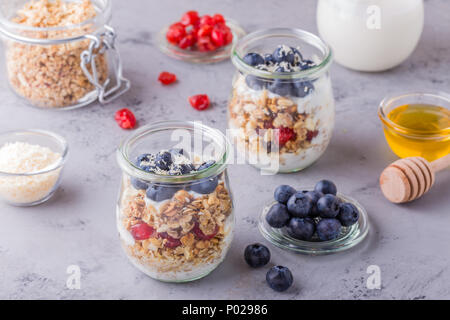Petit-déjeuner sain - pots de verre de flocons d'avoine avec des fruits frais, du yaourt et du miel, selective focus. Banque D'Images