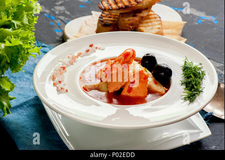 Soupe de poisson française Bouillabaisse aux fruits de mer, filet de saumon, crevettes, saveur riche, délicieux dîner dans un beau plat blanc. Close up. Banque D'Images