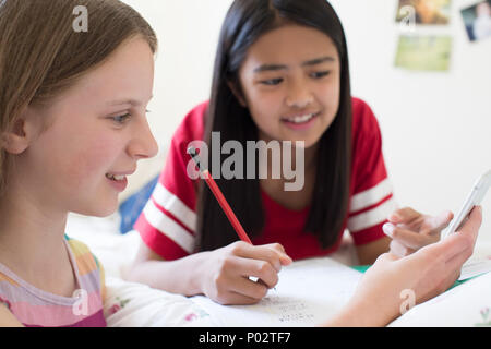 Deux Girls Lying On Bed Using Mobile Phone pour l'aide aux devoirs Banque D'Images