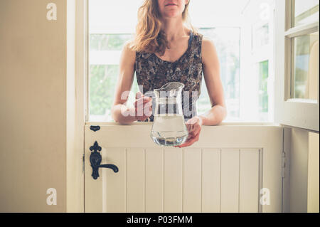 Une jeune femme se tient debout par une porte de l'écurie avec une cruche d'eau sur une journée ensoleillée Banque D'Images