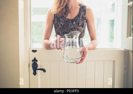 Une jeune femme se tient debout par une porte de l'écurie avec une cruche d'eau sur une journée ensoleillée Banque D'Images