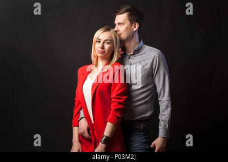 Belle jeune fille blonde blanche dans un costume rouge à la veste et chemisier blanc et grand brun accolades et embrassades sur arrière noir isolé Banque D'Images