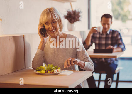 Cheerful woman eating salad et la causerie au téléphone Banque D'Images
