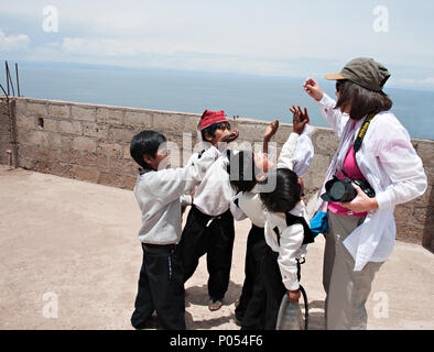 Les jeunes garçons se rassembler autour d'une sucrerie offerring et des bonbons dans le village à l'île de Taquile, le lac Titicaca. Pérou Banque D'Images