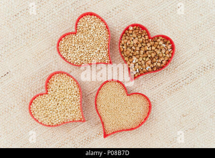 Quatre coeurs rouges remplis de céréales sans gluten, le quinoa, le millet, l'amarante et le sarrasin sur toile Banque D'Images