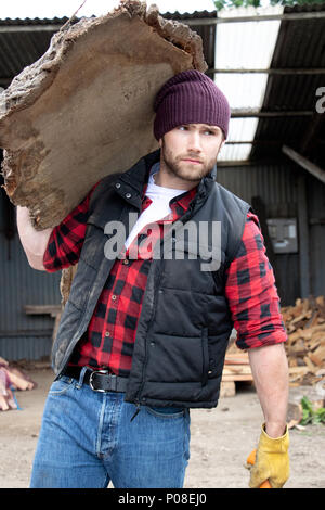 Bon à l'homme en chemise à carreaux carrying large planche en bois sur ses épaules en bois mill yard Banque D'Images