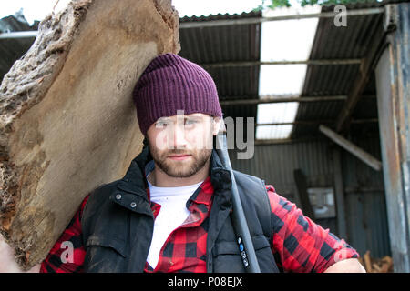 Bon à l'homme en chemise à carreaux carrying large planche en bois sur ses épaules en bois mill yard Banque D'Images