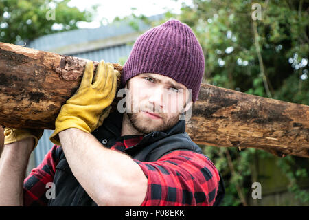 Bon à l'homme en chemise à carreaux carrying large planche en bois sur ses épaules en bois mill yard Banque D'Images