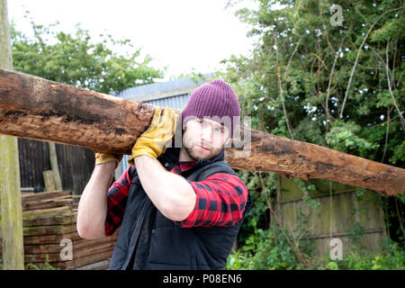 Bon à l'homme en chemise à carreaux carrying large planche en bois sur ses épaules en bois mill yard Banque D'Images