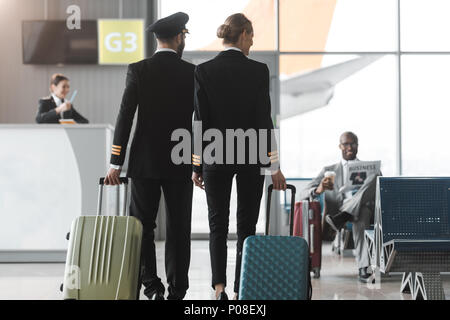 Vue arrière de l'homme et de femmes pilotes de marcher par airport hall avec des valises Banque D'Images