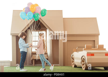 Kid présentant des ballons pour petite amie en face de maison en carton isolated on white Banque D'Images