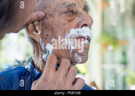Un homme âgé se raser la barbe par jeune homme du métier à la maison Banque D'Images