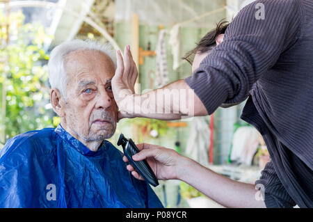 Un homme âgé se raser la barbe par jeune homme du métier à la maison Banque D'Images