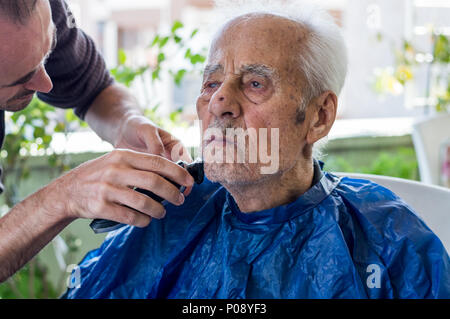 Un homme âgé se raser la barbe par jeune homme du métier à la maison Banque D'Images