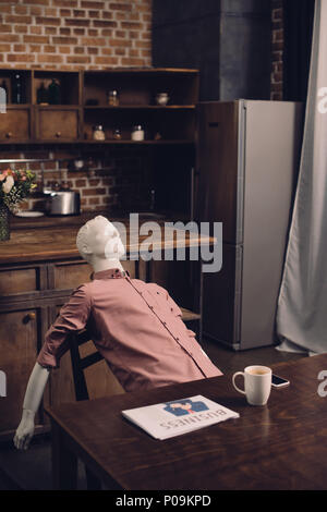 Vue rapprochée de mannequin à table avec tasse de café et des journaux dans la cuisine Banque D'Images