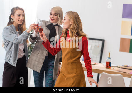 Les éditeurs de magazines de trinquer avec des verres de champagne in modern office Banque D'Images