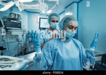 Médecin aidant à porter l'uniforme de la chirurgie chirurgien Banque D'Images