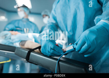 Portrait du médecin portant sur l'oxymètre de pouls doigt du patient en salle d'opération Banque D'Images