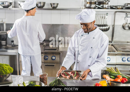 Multicultural chefs cooking la viande avec des légumes au restaurant de cuisine Banque D'Images