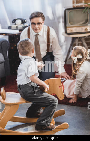 Adorable petit garçon assis sur le cheval à bascule et à jouer aux dominos avec père à fille, 50s style famille Banque D'Images