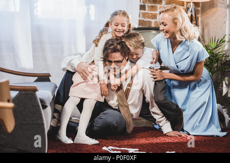 La famille de style rétro joyeux hugging tout en jouant aux dominos à la maison Banque D'Images